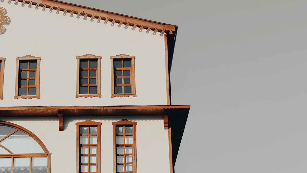 Fachada blanca de una vivienda tradicional con varios marcos de ventana de madera tallada en tono caramelo, muy decorados, bajo un cielo gris.